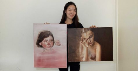 Junior Grace Park holds up her two award-winning paintings --