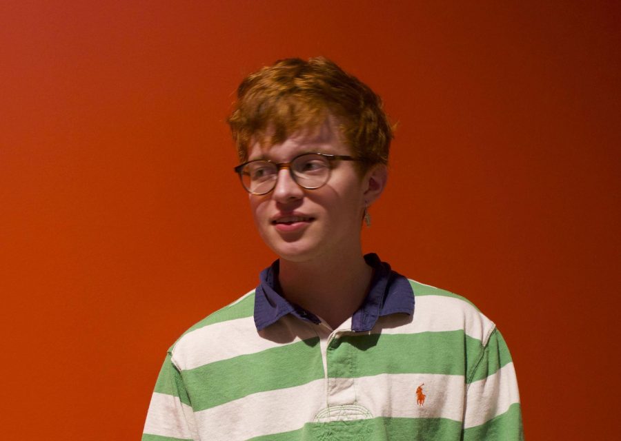 Standing in front of a red wall, singer-songwriter Robin Skinner, more commonly known as Cavetown, poses for the camera after his new albums debut. 