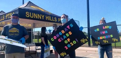 All wearing face masks as part of state COVID-19-related guidelines, social science teacher and co-ASB adviser David Fenstermaker (left), dance instructor Leiana Volen and yearbook adviser Lindsay Safe greet seniors as their cars come by the Sunny Hills parking lot as part of the May 8 drive-through event to pick up cap and gowns and Class of 2020 graduation yard signs. Fenstermaker handed out the yard signs. Video screen shot taken by Accolade photo editor Megan Shin.