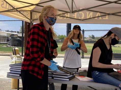 With blue gloves and face mask covering her mouth, math teacher Nicole Knutson (left) gets ready to hand off another yearbook to the next person pulling up to the drive-through distribution lane on the parking lot near the Performing Arts Center Tuesday afternoon. Yearbook adviser Lindsay Safe (center) supervises the operation while math teacher Mariam Tan uses a chromebook to confirm the names given to them. Photo taken by Accolade opinion editor Hope Li.