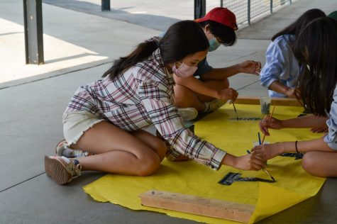 In the breezeway next to the 100s building, sophomore Ashley Kim (left) joins her fellow Associated Student Body [ASB] members in painting a letter on a poster to be used the next day, Friday, Aug. 20, in the Welcome Back assembly. The in-person gathering will be the first to take place in the gym since the coronavirus pandemic closed down schools in March 2020.