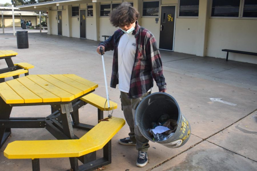 With a trash picker in his right hand and a trash container in the other, sophomore Adrian Ramirez demonstrates on Tuesday how he helps out after school. 
