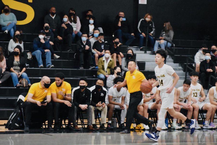 Point guard junior Chad Nguyen dribbles the ball in front of a sparse crowd as a result of the indoor audi- ence limit at a home game against Buena Park on Wednesday.