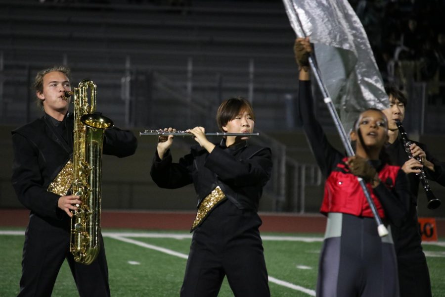 Baritone saxophonist junior Derek Thomson (left) and flutist sophomore Gray Lee blow their instruments, while Color Guard member sophomore Janessa Lima performs her choreography during “The Summit” performance for the state finals on Saturday, Nov. 19.