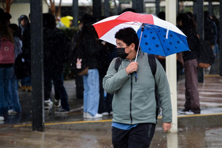 Senior Gabriel Tamayo holds a patriotic red, white and blue umbrella to shelter from the rainy weather near the 90s building on Tuesday, Jan. 10, during lunch. 