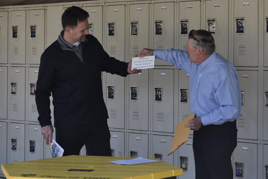 Principal Craig Weinreich (left) receives a plaque with an engraved inspirational quote from Sunny Hills Class of 1968 reunion committee co-chairman Brad Rawlins as a gift Thursday, March 9, during fourth period by the 30s wing. The quote reads, “Education Is The Passport To The Future Tomorrow Belongs To Those Who Prepare For Today.” Rawlins and nine other graduates from the Class of 1968 reunion committee met on the SH campus to glue nine inspirational quotes on the new benches and tables school officials had purchased through the groups $10,000 donation last summer.