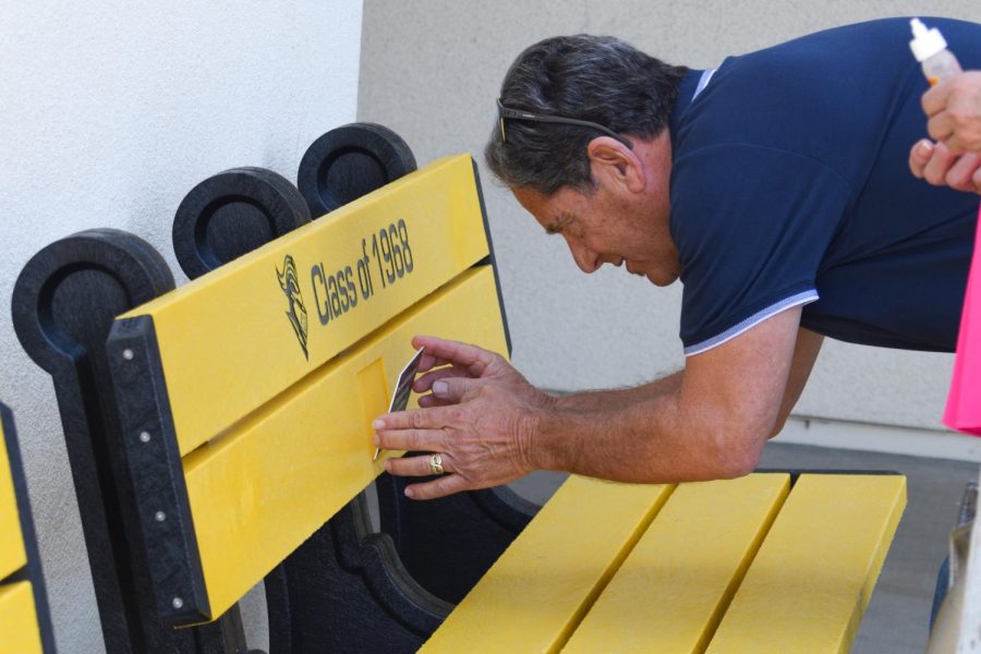 Class of 1968 reunion committee member Vince Citrano places the black plaque to glue on the center of the bench by the Lyceum Thursday, March 9. 
