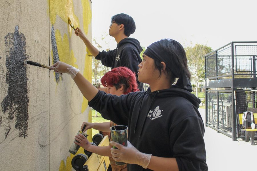 Senior Dylan Tran and two other Art Club members paint a black backdrop over a pencil sketch after school Tuesday, April 18, near the Lyceum entrance for the new mental health mural.