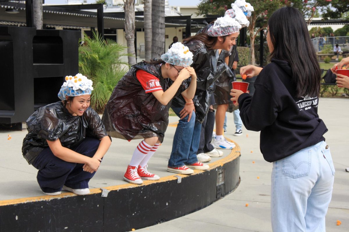 Along with the other five nominees for homecoming court, senior Denise Bravo (left) wears a shower cap with shaving cream on it, attempting to collect the cheeseballs that her partner senior Sarah Aurelio throws at her head in the quad on Thursday, Sept. 28. The court members participated in a total of two games during the week to promote themselves for the queen voting on Friday.