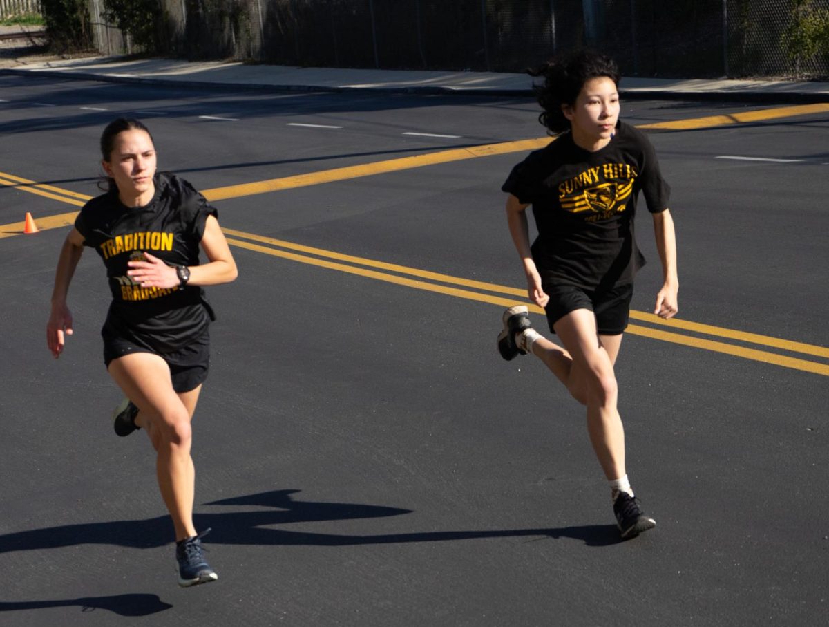 Sophomore Sophia Gentile (left) and junior Maya Kew-Layton practice sprinting uphill on Lancer Way toward the parking lot by the Performing Arts Center during sixth period on Monday, March 4.