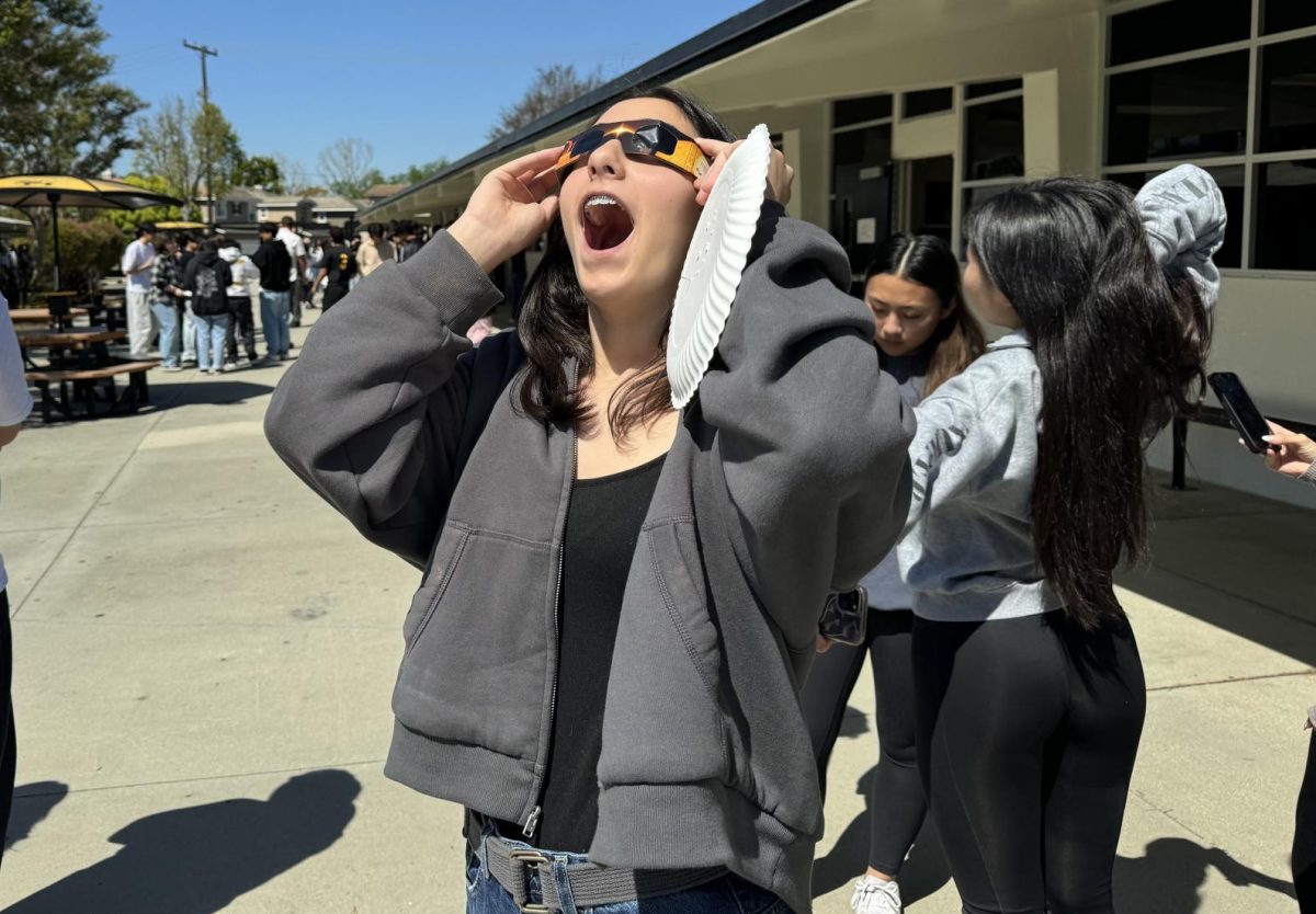 Junior Giulianna George looks toward the partial solar eclipse using special glasses to protect her eyes during her second period AP Environmental Science class by Room 112 on Monday, April 8. Science teacher Andrew Gartner was among the five science teachers by the 110s wing who let their students view the eclipse.