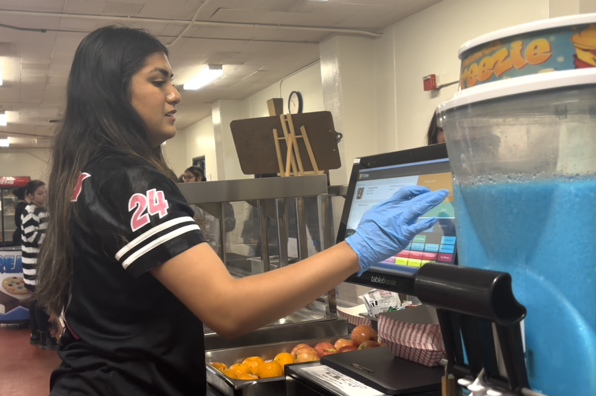 Student cafeteria worker senior Chloe Sepulveda uses the tablet while handing out food items to students during break on Friday, May 17, in the cafeteria.