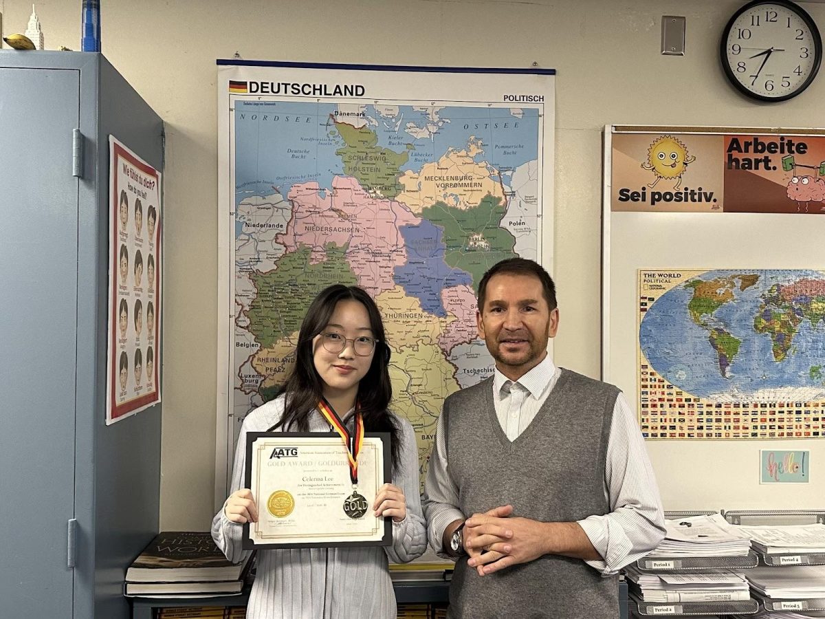 Junior Celerina Lee (left) wears her medal while holding up her National German Exam certificate, both of which were given to her from her German 3 honors teacher, Sergey Artemyev, on Thursday, May 9. The awards recognize her high marks from the National German Exam.