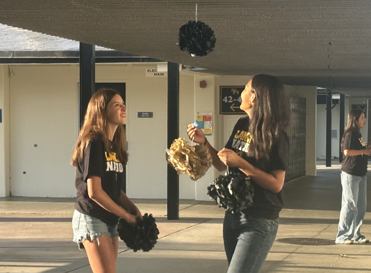 Associated Student Body [ASB] members sophomore Cambria Dominguez (left) and junior Kayla Thienprasiddhi look at one of the stringed decorations they put up that hangs off the awning outside the 40s wing before the first day of school starts on Monday, Aug. 12. The ASB installed decorations before zero period to welcome students and show school spirit.