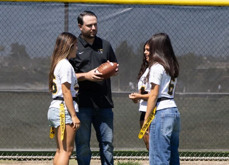 Girls flag football coach Dylan Kuhn gives a pep talk to his three quarterbacks, freshman Soliao Arredondo (left), junior Samantha Apolinar and sophomore Amelia Herbert, on the field during lunch before their Wednesday, Sept. 11, game against Troy High School.