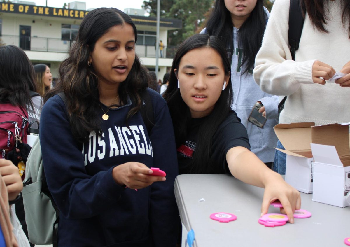 Seniors Sienna Shah (left) and Anabelle Kim sort through the various compact mirrors with breast cancer awareness stickers in front during break on Monday, Oct. 14, in the quad. Monday’s display table was among the initial set of activities that the Associated Student Body [ASB] organized as part of Breast Cancer Awareness week.