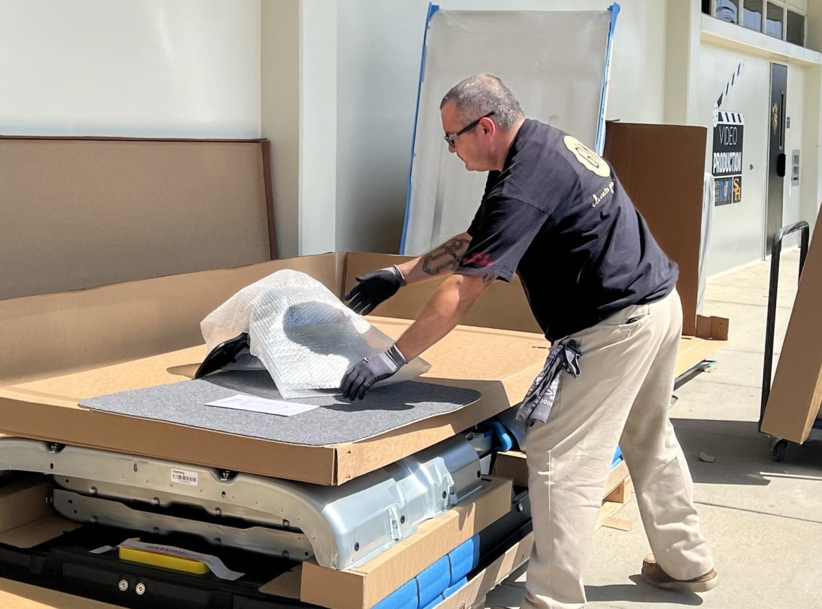 Mike Delgado, an installer from Irvine-based G|M Business Interiors, unpacks on Tuesday, Sept. 24, during fourth period boxes containing new furniture ordered for Room 136, which houses the Regional Occupation Program’s video production classes and where the weekly videos of “Sunny Side Up” are recorded. Teacher Daniel Flores has been overseeing a major remodeling of his classroom, which began over the summer when the darkroom — used for developing film from older cameras back when photo classes were taught in Room 136 — was removed to make way for a more modern look.