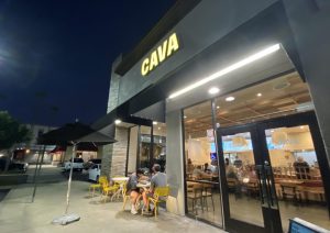 Outside Cava’s Brea location on 103 W Imperial Hwy, a small space for outdoor seating allows customers to dine outside under and a neon yellow sign at the entrance with “CAVA” written in capital letters. Cava’s Brea location opened on Friday, May 10.