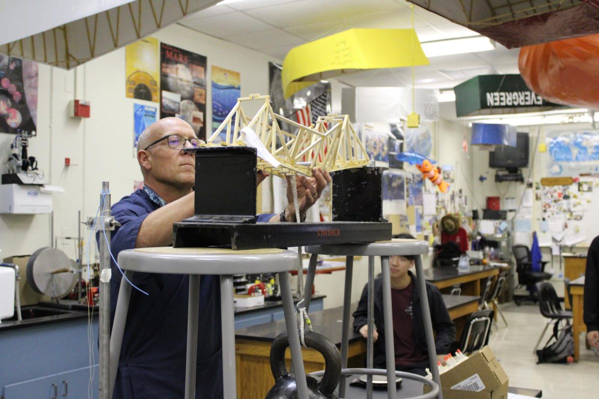 Science teacher Chris Peoples adjusts a wooden bridge in Room 155 on Monday, Nov. 4, during fourth period after attaching a 60-pound weight to test information that he and his class have covered and to prepare students for a boat project later in the school year for extra credit. The bridge, made by seniors Chase Lee and Matthew Mendoza in Peoples’ fourth period physics class, failed to hold the weight because of a lack of construction. 