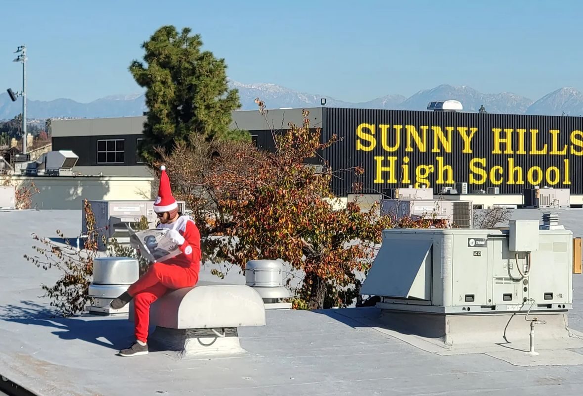 A Sunny Hills staff member dresses up as an elf and reads the Nov. 18, 2022, Accolade newspaper issue while sitting atop the roof of one of the campus buildings on Dec. 21, 2022.