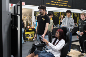 Senior Sebastien Roque shows an eighth-grade visitor how to use the racing simulator during the Parks Junior High preview day on Friday, Jan. 10, in the gym.