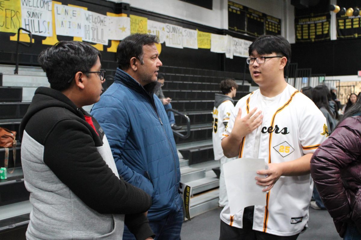 Associated Student Body [ASB] president senior Sean Lee (right) talks about the program he represents in the gym with a visiting eighth-grader and his parent during the Tuesday, Jan. 21, Open House. All ASB members wore baseball jerseys for identification during the event.