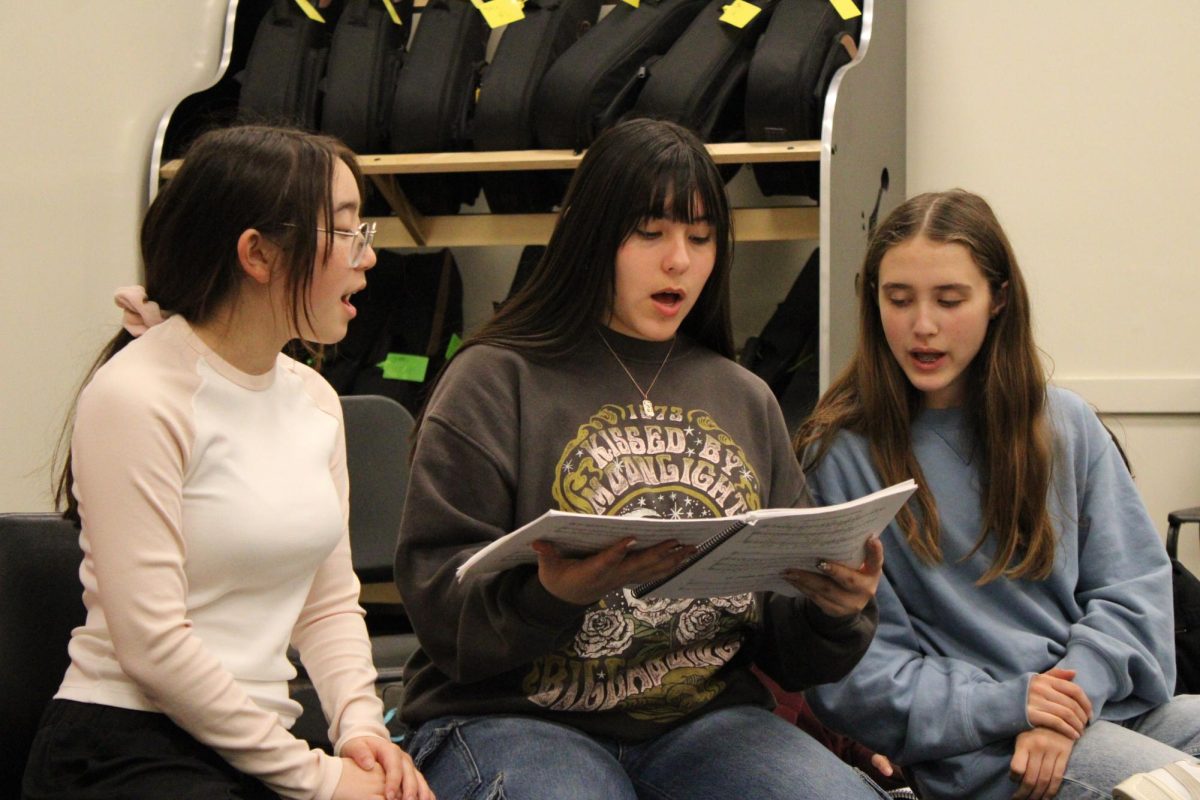 Junior Mia Cho (left), sophomore Celeste Lopez-Garduno and freshman Ellie Klausman share a “Joseph and the Amazing Technicolor Dreamcoat” sheet music to use while singing.