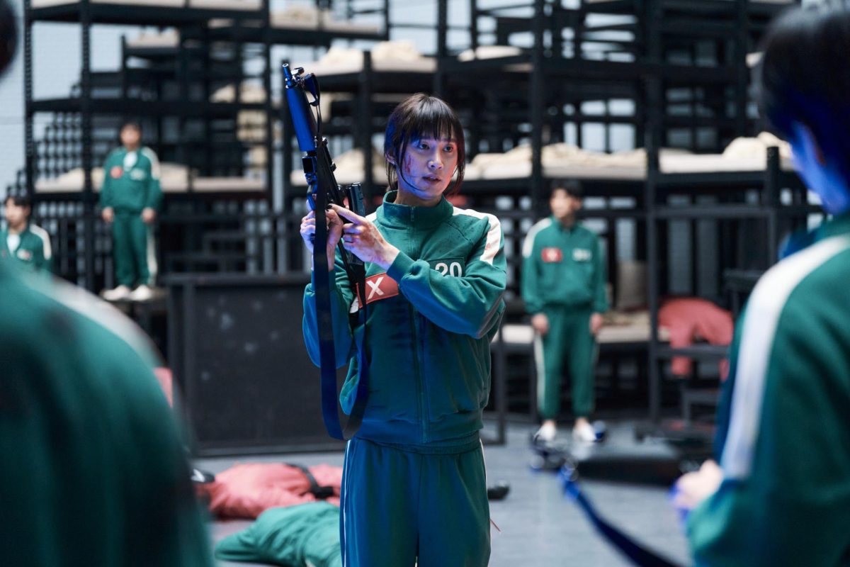 Park Sung-hoon (center) acts as Player 20, who carries a machine gun as she discusses with contestants how to ambush the shooters in Episode 7.    