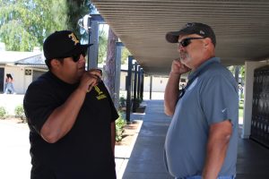 New campus supervisor Jason Hughes (right) demonstrates how he would listen to supervisor liaison Randall Avalos’s walkie-talkie message in the hallway near the 10s wing on Friday, April 11.