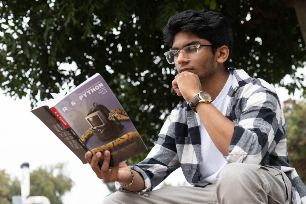 Senior Jai Patel holds open the 310-page book he had co-authored during his 2024 Boeing summer internship. Statistical Programming Essentials: R & Python is available for purchase on Amazon for $22.99. 