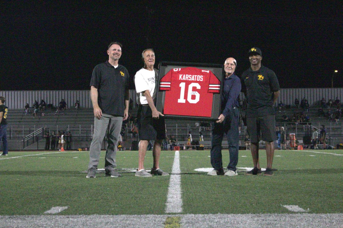 Former coaches Ralph Trigstead (left of jersey) and Tim Devaney (right of jersey) hold up former Lancer football player Jim Karsatos’ jersey from Ohio State University in commemoration of his achievements. This event took place during the halftime of football’s first home game of the season on Friday, Aug. 29, at the Buena Park High School Stadium.