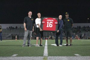 Former coaches Ralph Trigstead (left of jersey) and Tim Devaney (right of jersey) hold up former Lancer football player Jim Karsatos’ jersey from Ohio State University in commemoration of his achievements. This event took place during the halftime of football’s first home game of the season on Friday, Aug. 29, at the Buena Park High School Stadium.