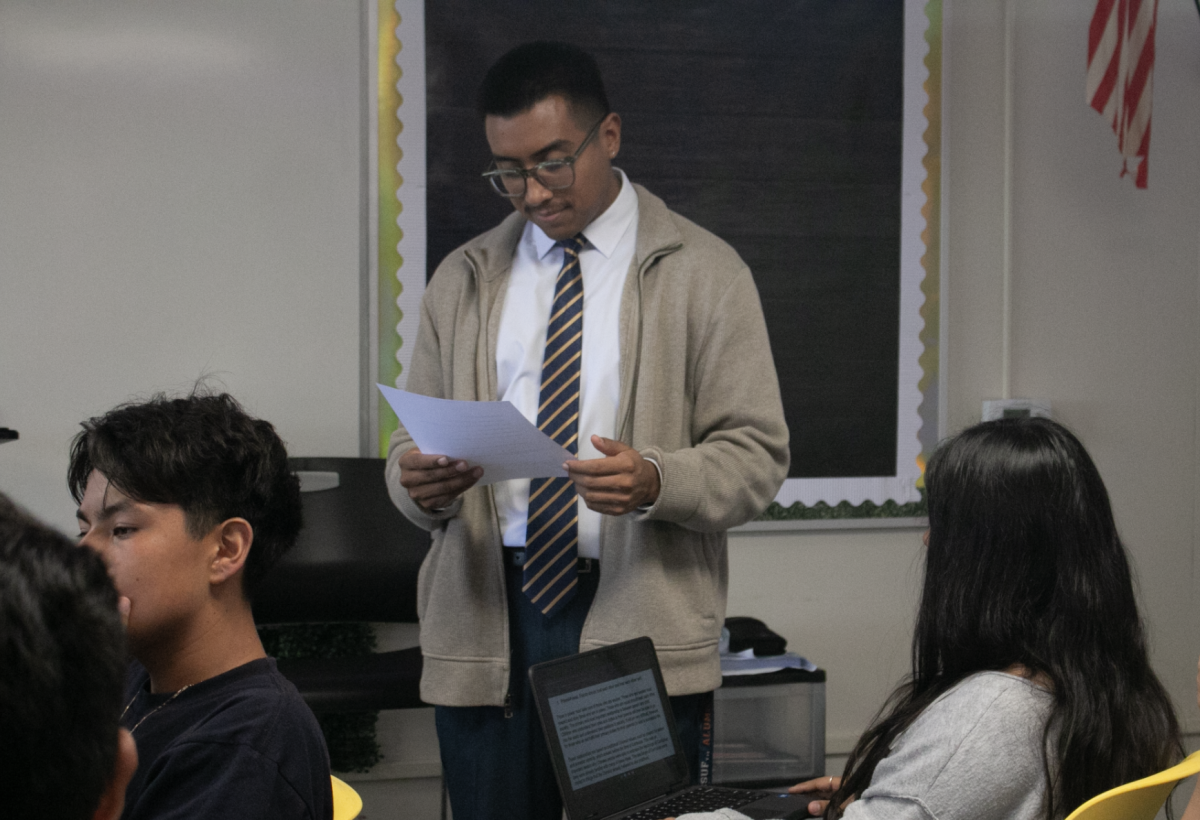 Social science teacher Marcus Reveles holds up a paper assignment about world religions to explain to his students about how to answer the question during fourth period World History in Room 24 on Sept. 5. 