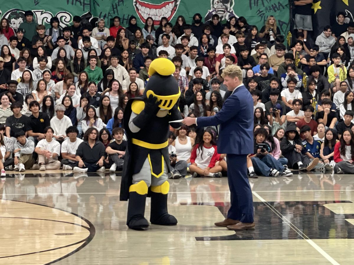 Senior Aaron Green shows the new Lancer mascot a piece of paper revealing the winner of the class homecoming dance competition during the first assembly on Thursday, Oct. 30.  (Siriana Thampi)
