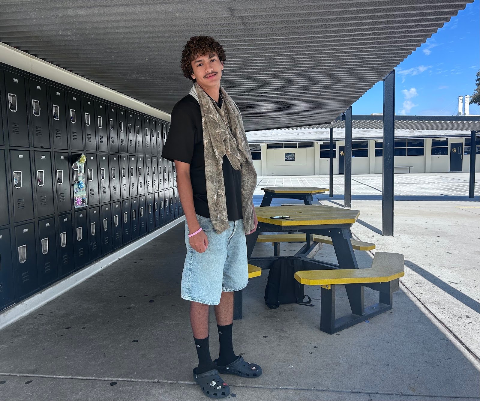 Junior Nathan Hernandez stands near the 90s buildings on Thursday, Oct. 9, and shows off his outfit: a T-shirt, jorts and a hoodie hung around his neck.
