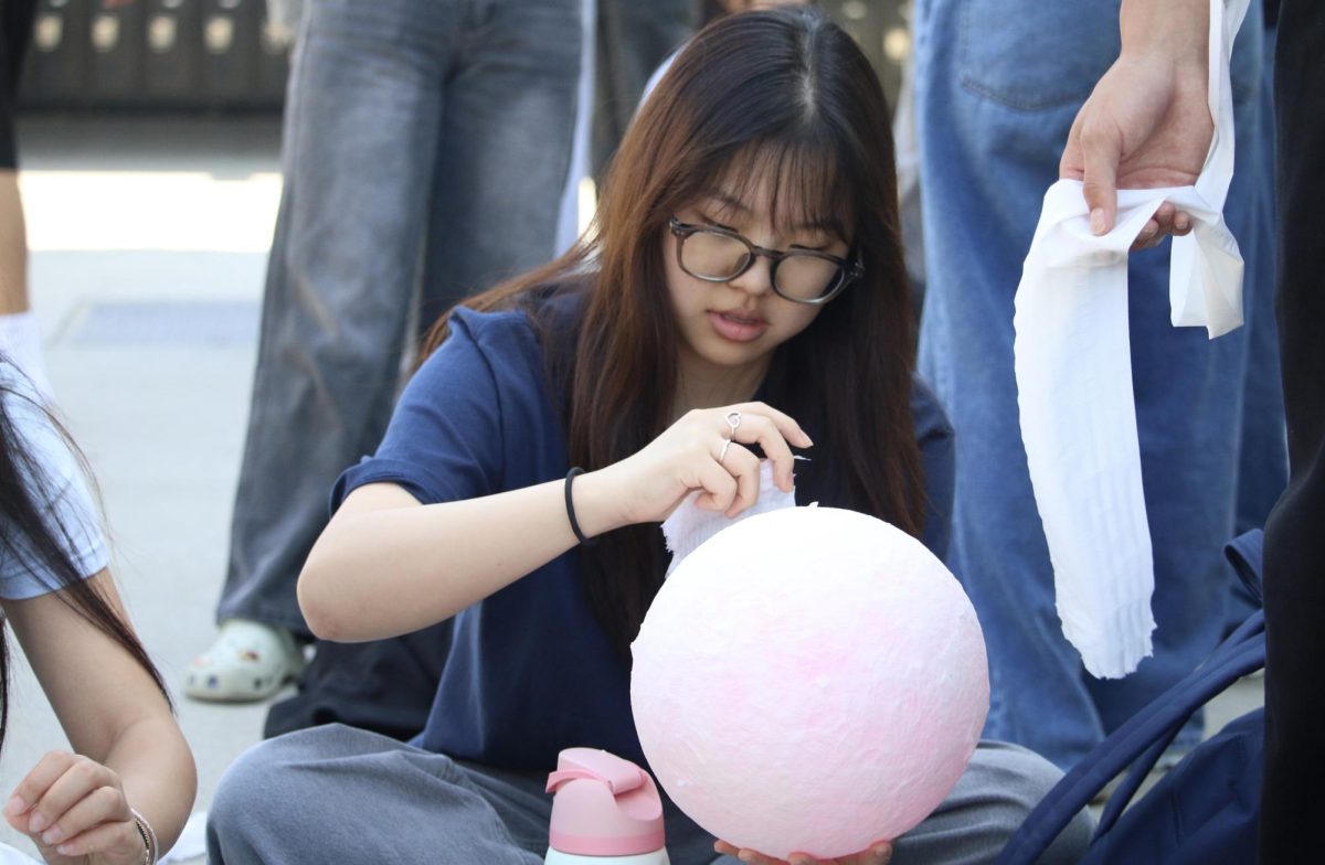Senior Allison Rah places a tissue onto a balloon to make a traditional Korean mask for her Korean class during fourth period on Tuesday, March 24, in the quad.